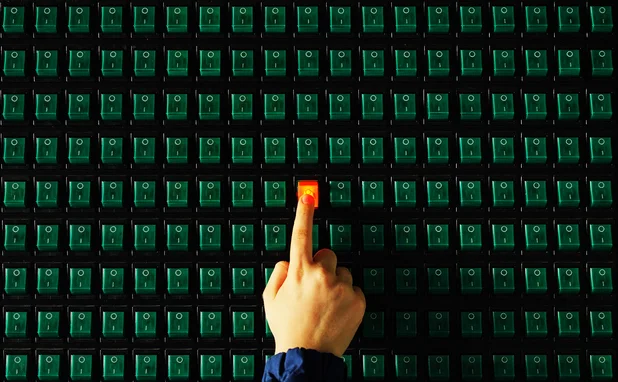 A finger switches on a button, which lights up red, on a panel full of green buttons that are switched off