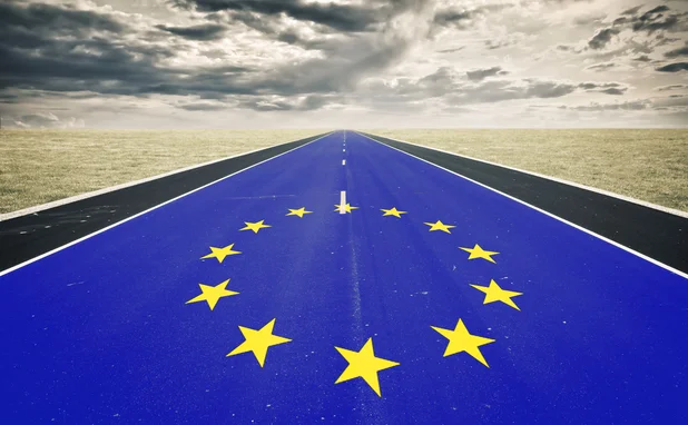 A very long road, with tarmac painted like the EU flag, stretches into the distance