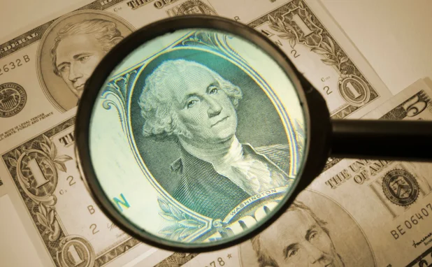 a dollar bill has a magnifying glass hovering over it to denote analysis