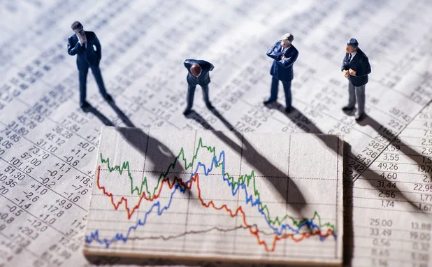 Small plastic figurines of businesspeople look quizzically at a large financial chart