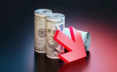 A red down arrow leaning against two rolls of US dollar notes 