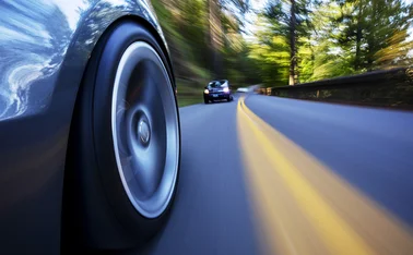 Close-up of the wheel of a car speeding ahead of others on a blurred country road