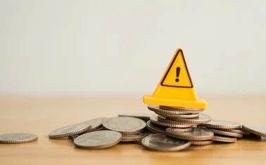 A yellow warning traffic cone sits on top of a pile of coins