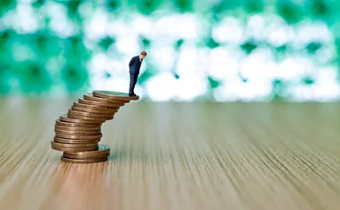 Businessman figurine standing on stack of coins that looks like it's about to topple over