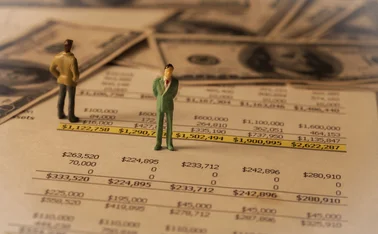 Tiny models of businessmen stand on some sheets of financial plan pages