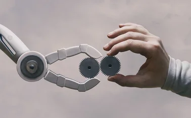 A robot and a human hand both hold cogs that tesselate