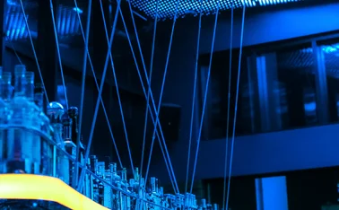 Blue-lit modern bar interior with illuminated ceiling panels, reflective glass bottles and sleek architectural details, creating a futuristic atmosphere with vibrant blue and yellow lighting