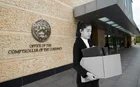 A woman stands outside the OCC building holding a cardboard box, because she has lost her job. Image is created, not real-life.