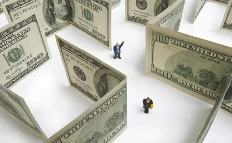 Two plastic models of businesspeople navigate through a maze of $100 banknotes
