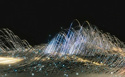 A dynamic abstract visualisation of glowing fibre-optic strands and light trails against a dark background, representing data flow, digital connectivity and high-speed network technology.