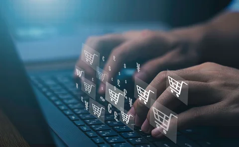 fingers typing on a keyboard, overlaid with an image of many different currency symbols and shopping cart icons