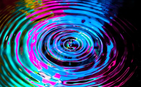 A droplet creates a ripple effect in multi-colours
