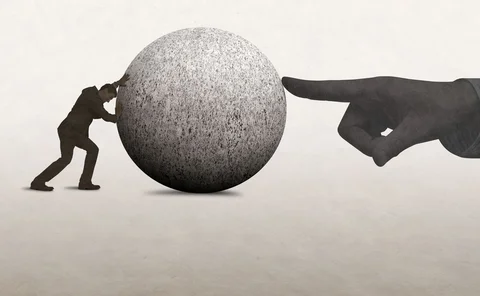 A man pushes a large concrete ball, while a hand on the other side tries to stop it moving