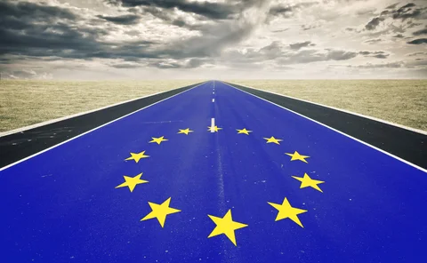 A very long road, with tarmac painted like the EU flag, stretches into the distance