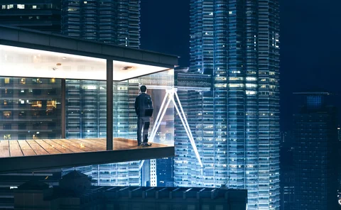 Business professional on rooftop balcony overlooking illuminated city skyline at night, modern urban architecture and corporate concept.