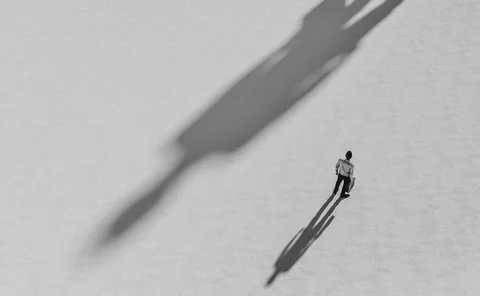 A large, long shadow is cast ominously next to a businessman