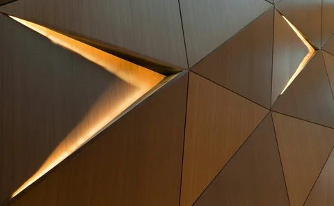 Abstract geometric wood wall with illuminated triangular openings and warm metallic textures