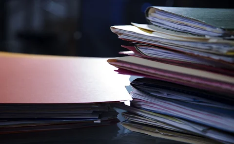 Piles of paper folders containing documents on top of a desk