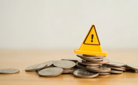A yellow warning traffic cone sits on top of a pile of coins