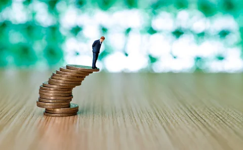 Businessman figurine standing on stack of coins that looks like it's about to topple over