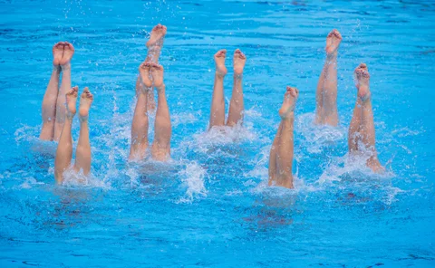 Eight pairs of legs, belonging to synchronised swimmers, stick upright from the water in a blue pool 
