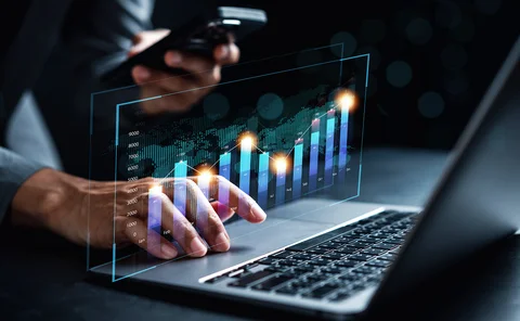Analyst holds a smartphone in his hand and examines data overlaid on background of laptop