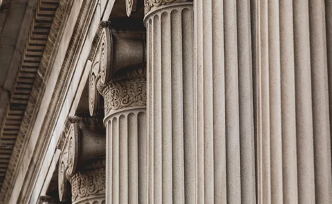 Close-up of ornate classical stone columns and architectural detailing on a courthouse or institutional building, symbolising law, regulation and financial governance.