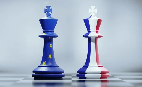 Two king chess pieces textured with French and European Union flags on black and white chessboard.