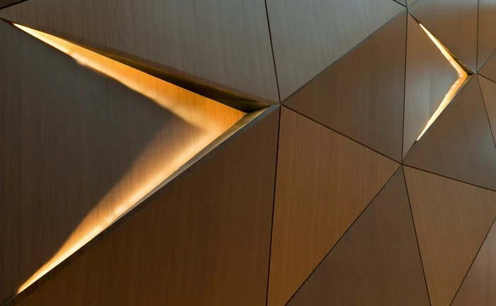 Abstract geometric wood wall with illuminated triangular openings and warm metallic textures