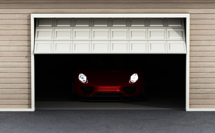 Garage door slowly opens to reveal high-tech car inside, with headlights on