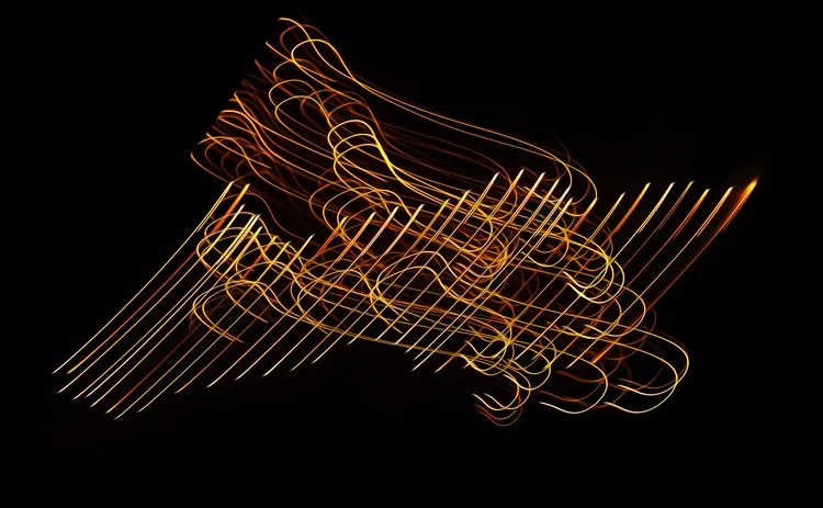 Abstract light painting with golden streaks and swirling lines on a black background, creating a dynamic and chaotic motion effect.