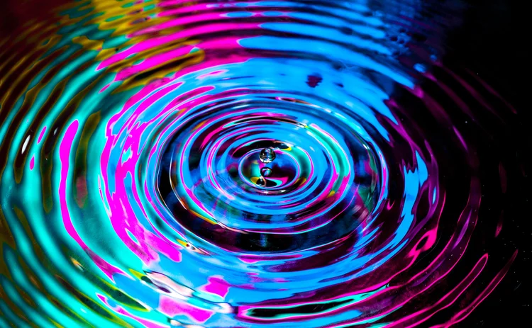 A droplet creates a ripple effect in multi-colours