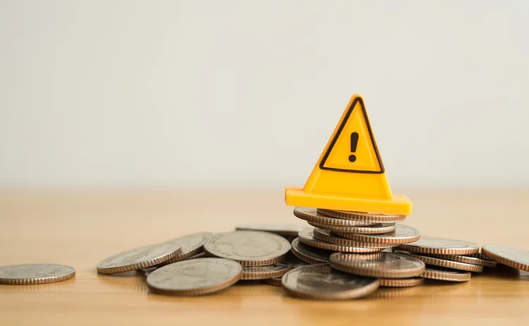 A yellow warning traffic cone sits on top of a pile of coins