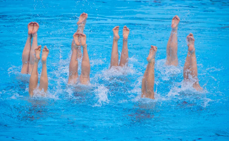 Eight pairs of legs, belonging to synchronised swimmers, stick upright from the water in a blue pool 