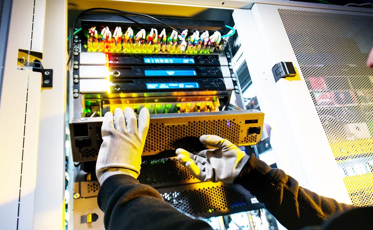 Gloved engineer fixes computer hard drive in server stack
