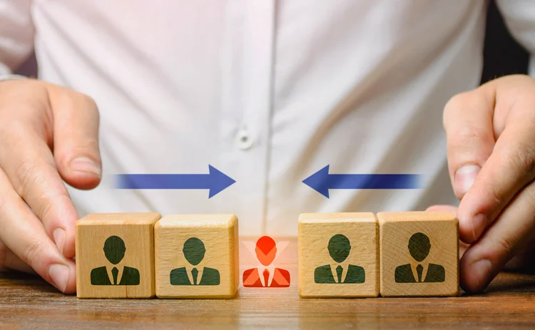Businesspeople on wooden blocks being moved by hands inwards to crush or displace a businessperson in red with cross depicting a veto