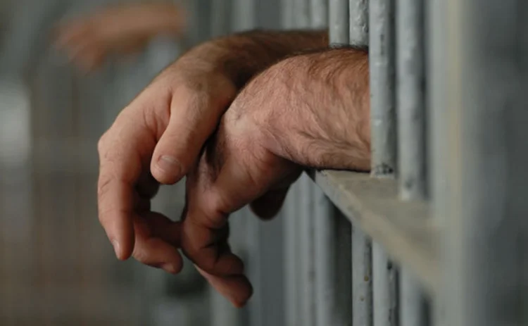 A pair of hands resting on prison bars