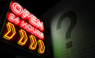 “Open 24 hours” neon sign with a shadowy question mark on the adjacent wall