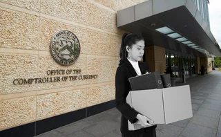 A woman stands outside the OCC building holding a cardboard box, because she has lost her job. Image is created, not real-life.