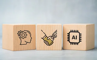 Three wooden blocks with a robot shaking a human hand, a brain with mechanical cogs, and an AI cube