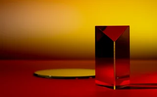 Abstract geometric composition featuring a red glass prism and circular reflective surface against a red and yellow gradient background, illuminated by warm light for a minimalist, modern art effect.