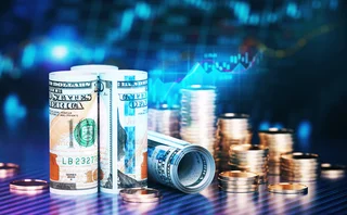 Dollar banknotes and coins in front of a blurry, blue financial data chart
