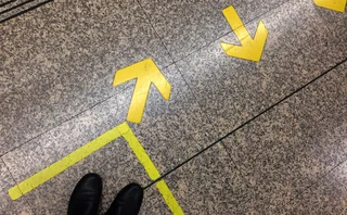 Top view of passenger’s feet standing in front of painted yellow box and directional arrows on a train station floor