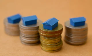 Small blue toy houses rest on top of columns of coins