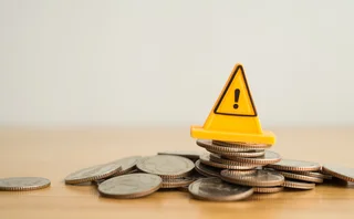 A yellow warning traffic cone sits on top of a pile of coins