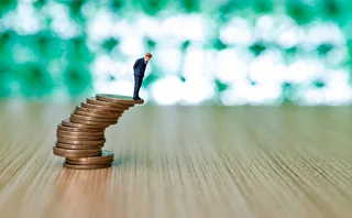 Businessman figurine standing on stack of coins that looks like it's about to topple over