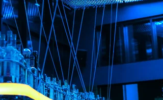 Blue-lit modern bar interior with illuminated ceiling panels, reflective glass bottles and sleek architectural details, creating a futuristic atmosphere with vibrant blue and yellow lighting