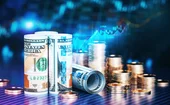 Dollar banknotes and coins in front of a blurry, blue financial data chart