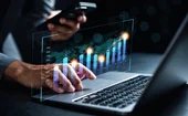 Analyst holds a smartphone in his hand and examines data overlaid on background of laptop
