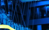 Blue-lit modern bar interior with illuminated ceiling panels, reflective glass bottles and sleek architectural details, creating a futuristic atmosphere with vibrant blue and yellow lighting